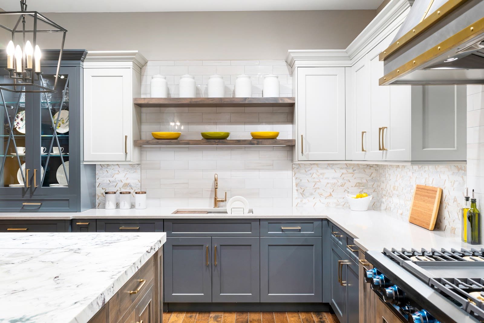 Two-tone kitchen with marble waterfall island and brass hood