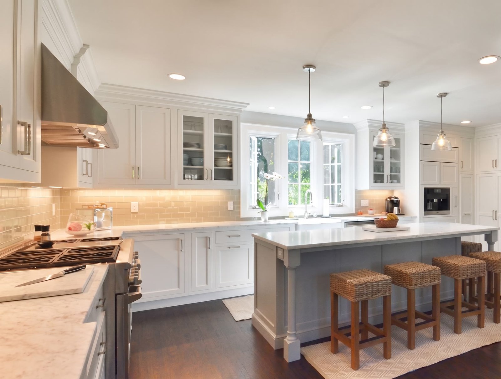White kitchen with a grey island, marble counters, and woven stools by Today's Kitchens